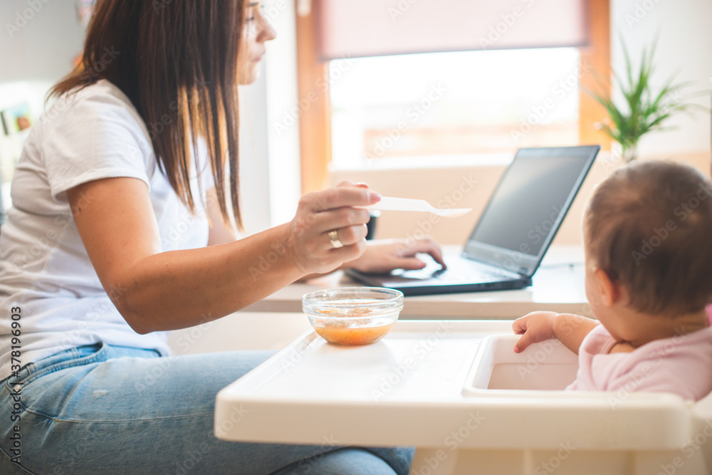 Mother feed her little daughter with a spoon and search on internet food recipes