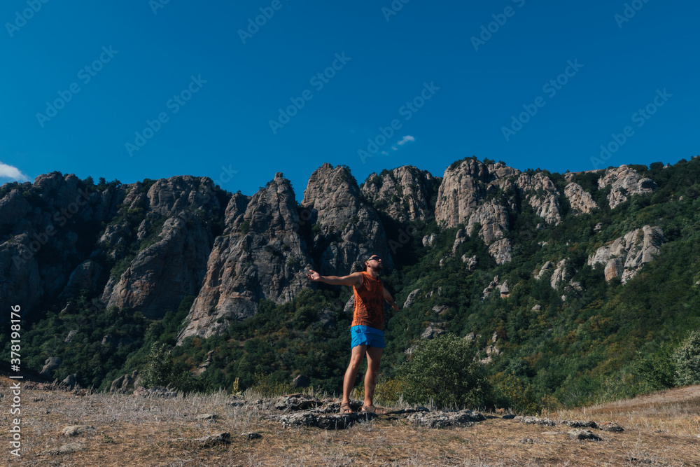A man tourist stands on a rock against the backdrop of a cliff and mountains