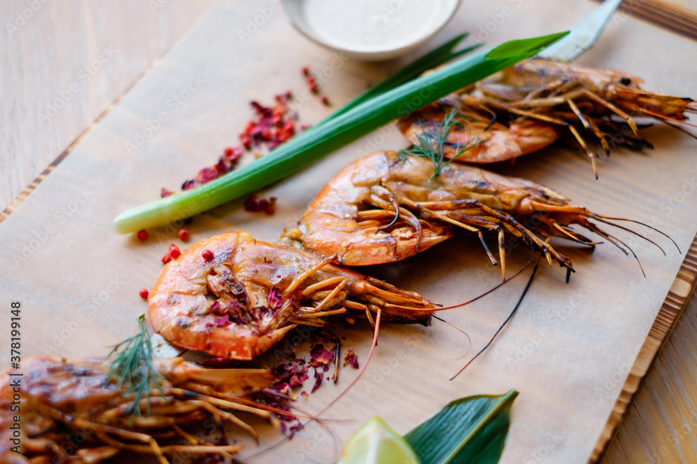 Delicious prawn on metall spit. Seafood on decorated wooden board. Grilled shrimps on metal skewer close-up. Delicious prawn on metall spit. Seafood on decorated wooden board. Grilled shrimps on metal skewer close-up.