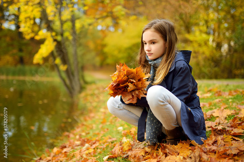 Adorable young girl having fun on beautiful autumn day. Happy child playing in autumn park. Kid gathering yellow fall foliage.