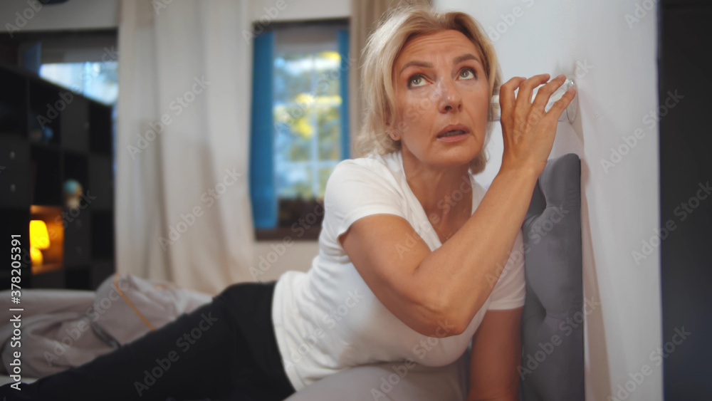 Senior woman eavesdropping through wall of room through glass cup Senior woman eavesdropping through wall of room through glass cup