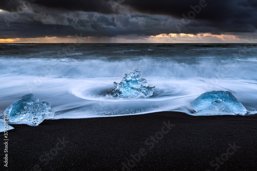 Morceaux de glaçons sur la plage de sable noir de Jokulsarlon avec un ciel orageux
