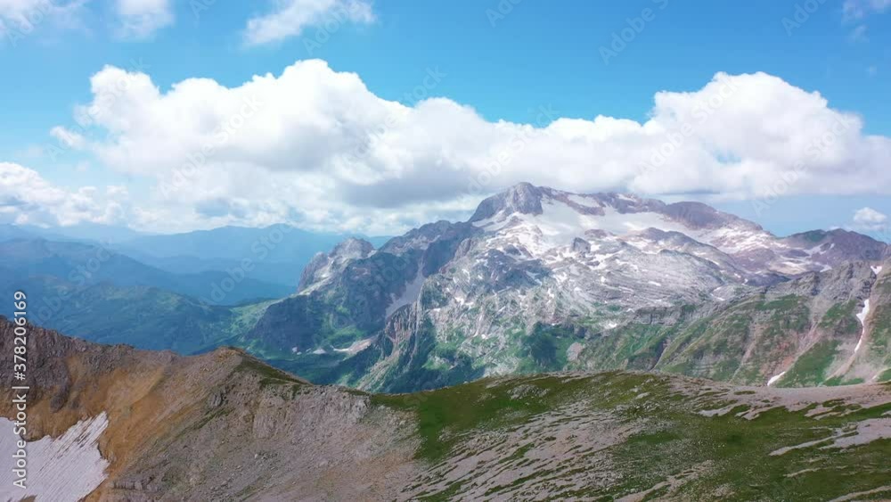 Aerial view from Oshten peak of stunning majestic nature of Caucasus to Mountain Fisht , covered with snow stones and grass under white clouds in blue sky. Sun glare sunraise in summer, Adygea, Russia Aerial view from Oshten peak of stunning majestic nature of Caucasus to Mountain Fisht , covered with snow stones and grass under white clouds in blue sky. Sun glare sunraise in summer, Adygea, Russia