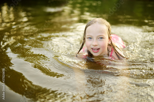 Fototapeta Naklejka Na Ścianę i Meble -  Cute little girl wearing swimsuit playing by a river on hot summer day. Adorable child having fun outdoors during summer vacations.