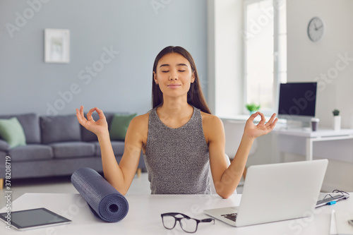 Relaxed business lady sitting at desk in her office taking break from work and practicing meditation photo