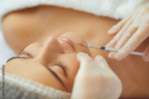 Cosmetologist making botox filler injection in female lips with syringe in beauty salon photo