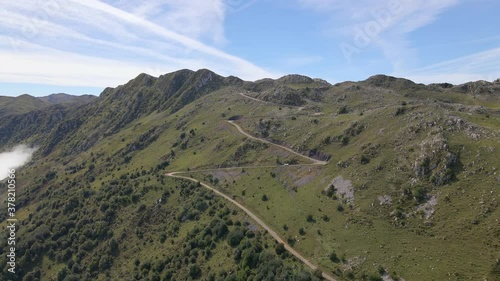 Drone pull back shot of steep Angliru road switchbacks up rocky green mountain photo