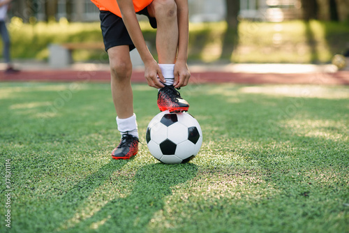 Close up boot of football player which puts his leg on ball and tying shoelace on soccer stadium on the training.