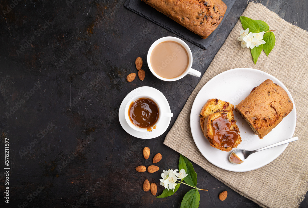Homemade cake with raisins, almonds, soft caramel and a cup of coffee on a black concrete background. top view, copy space. Homemade cake with raisins, almonds, soft caramel and a cup of coffee on a black concrete background. top view, copy space.
