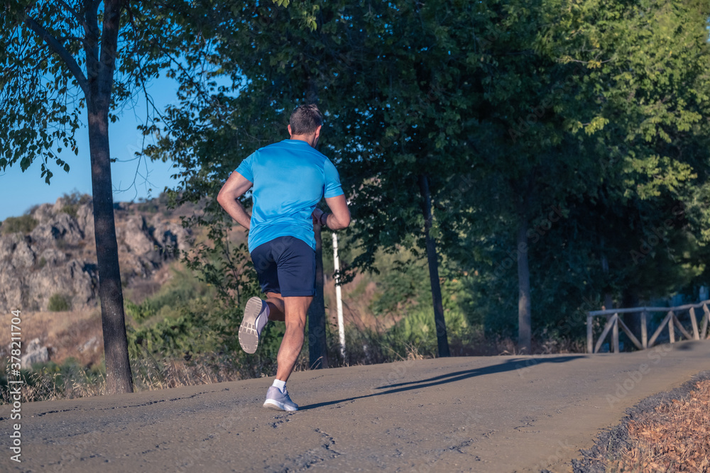 Fototapeta premium Young man in blue t-shirt running through a park