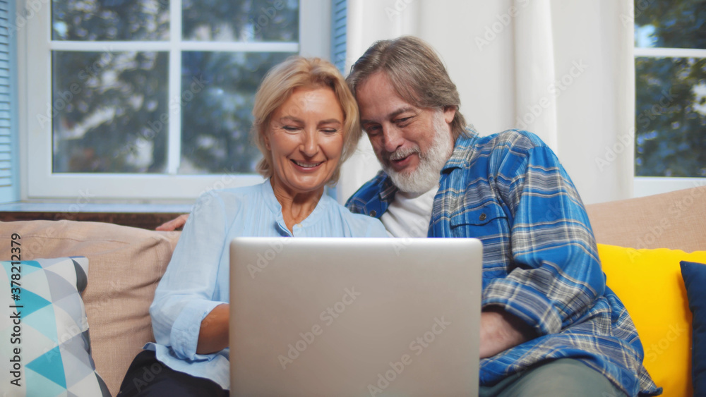 Senior couple relaxing and using laptop together sitting on sofa in living room at home Senior couple relaxing and using laptop together sitting on sofa in living room at home