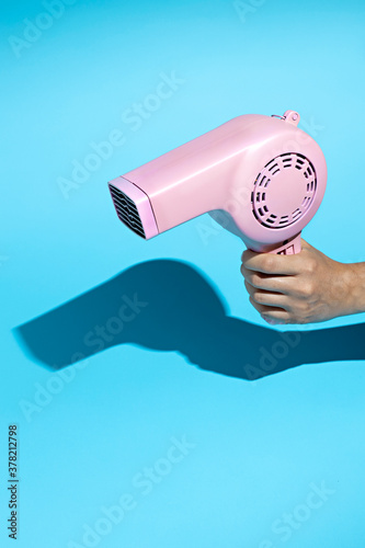 Layout made with pink hairdryer on blue background. Retro vintage 60's and 70's aesthetic with summer shadows. Minimal hairdressing concept. Flat lay. photo