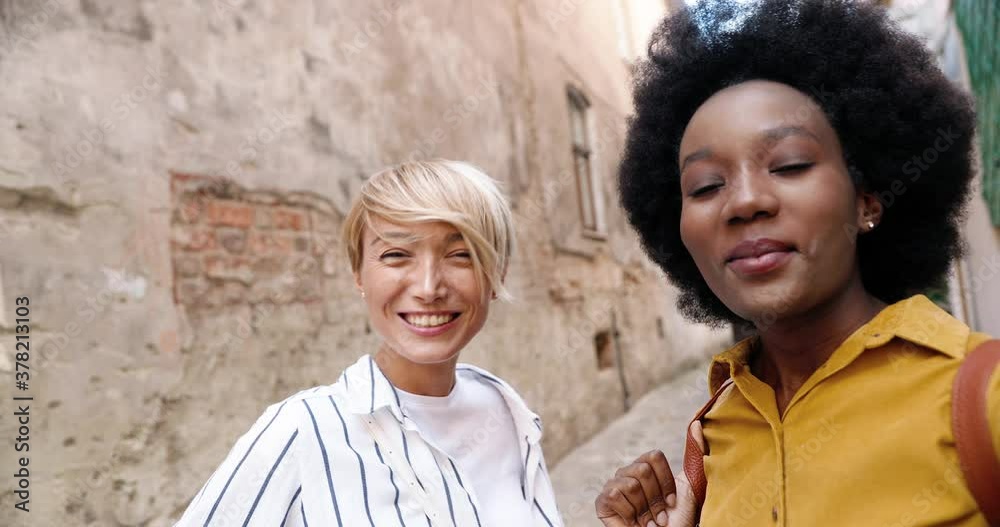POV of joyful multi-ethnic females talking on video chat outdoor. Close up portrait of happy beautiful Caucasian and African American girls chatting through webcam while standing in city Urban concept POV of joyful multi-ethnic females talking on video chat outdoor. Close up portrait of happy beautiful Caucasian and African American girls chatting through webcam while standing in city Urban concept