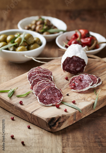 Sliced french salami with fresh rosemary and olives on rustic wooden background. 