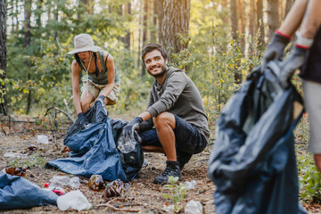 Young man looking on his friend while collecting trash and plastic in forest