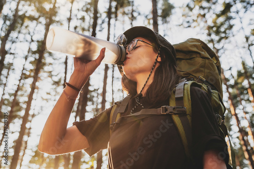 Low angle view of beautiful female hiker drinking water in forest at sunset