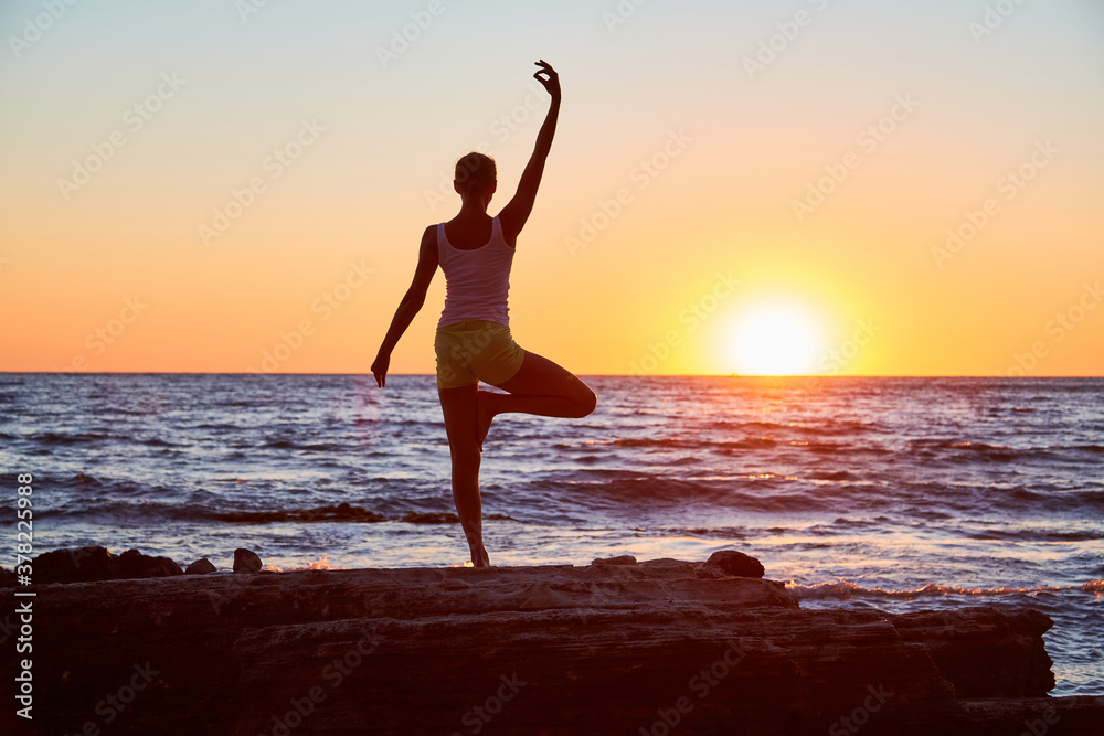 Fit female standing in yoga position. Sunset over sea landscape. Yoga meditation. Pilates and active lifestyle concept