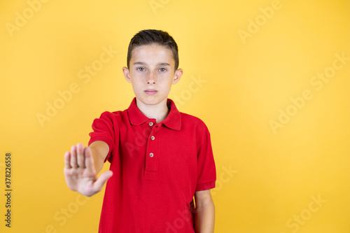 Young beautiful child boy over isolated yellow background serious and doing stop sing with palm of the hand.
