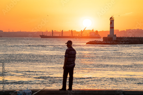 At sunset, a man is watching the sunset on the Kadikoy shore, while a freighter passes by.