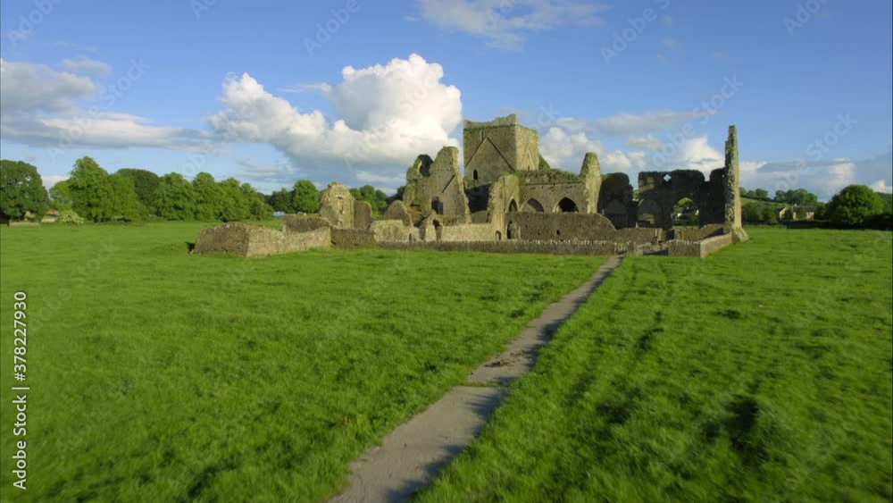 Wide aerial, woman hikes to castle ruins in Ireland Wide aerial, woman hikes to castle ruins in Ireland