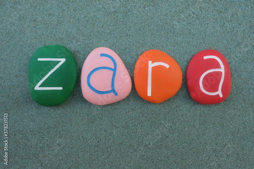 Fotografi Zara, female given name composed with multicolored stone letters over green sand