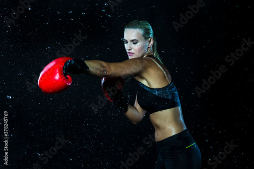 Portrait of Professional Active Female Boxer  Posing with Red Gloves In Water Droplets Against Black Background. © danmorgan12