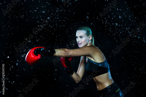 Active Female Boxer  Posing with Red Gloves In Water Droplets Against Black Background. © danmorgan12