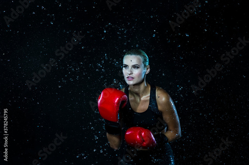 Female Boxer  Posing with Red Gloves In Water Droplets Against Black Background. © danmorgan12
