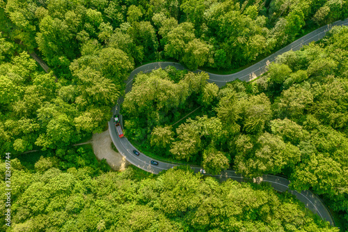 Aerial view of a green forest with a tractor on its leading through street slowing a row of cars behind it - traffic jam at a beautiful travel day © allessuper_1979