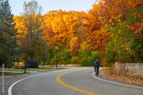 Bicyclist riding on curvy road during a beautiful autumn day with leaves turning colors