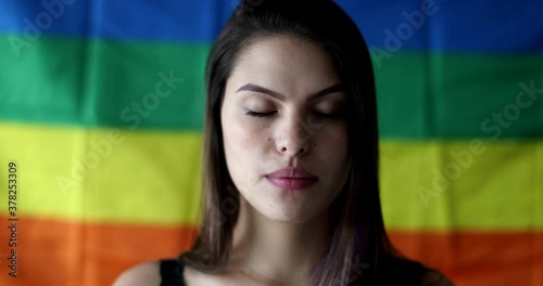 Portrait of LGBT woman standing in front of rainbow flag. Girl taking deep breath smiling at camera photo