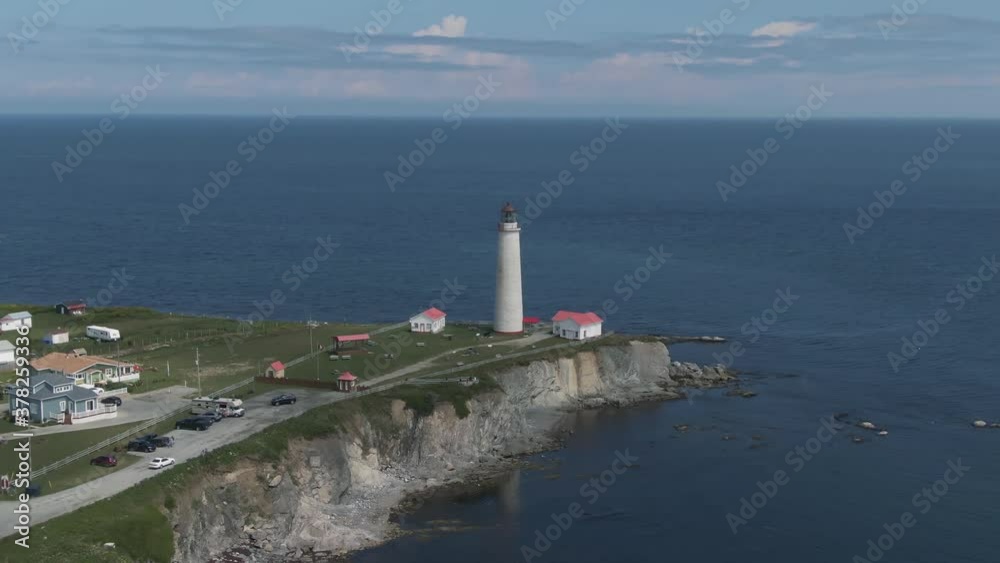 Calm Waters Of Saint Lawrence River Surrounding The Cap-des-Rosiers Lighthouse Situated Near The Village Of Cap-des-Rosiers In Gaspe Peninsula, Quebec, Canada. - aerial ascending shot Calm Waters Of Saint Lawrence River Surrounding The Cap-des-Rosiers Lighthouse Situated Near The Village Of Cap-des-Rosiers In Gaspe Peninsula, Quebec, Canada. - aerial ascending shot