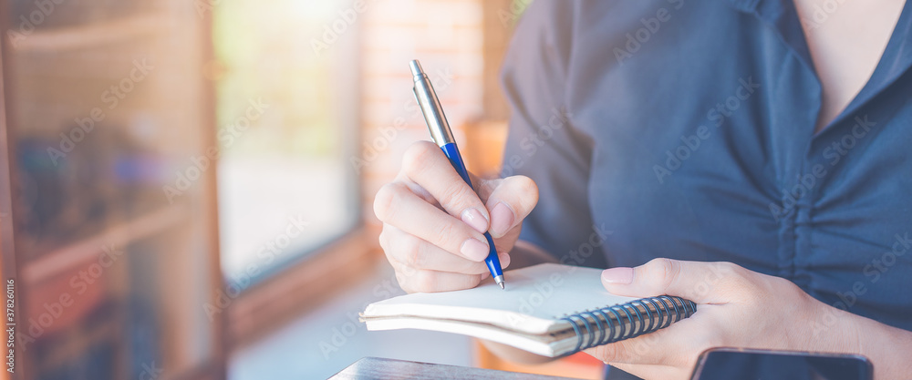 Woman is writing on a notebook with a pen in the office.