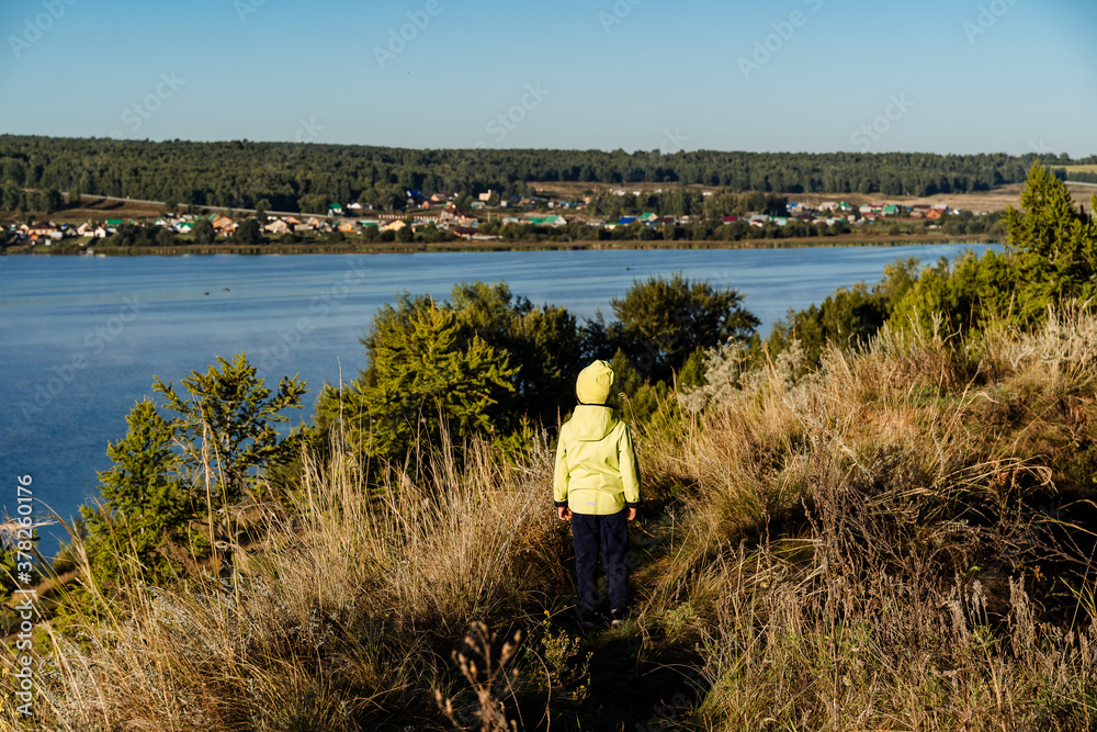 A little boy in a jacket walks along the lake in nature. The child explores the world around them. Independent walks in the fresh air. Children's tourism. Meet the morning on the beach.