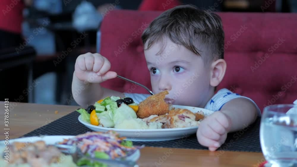 Portrait of a child boy eats mashed potatoes with salad, tomatoes, broccoli and red sauce in a light domestic room. A small child is twisting spaghetti on a fork and eating meal. Portrait of a child boy eats mashed potatoes with salad, tomatoes, broccoli and red sauce in a light domestic room. A small child is twisting spaghetti on a fork and eating meal.