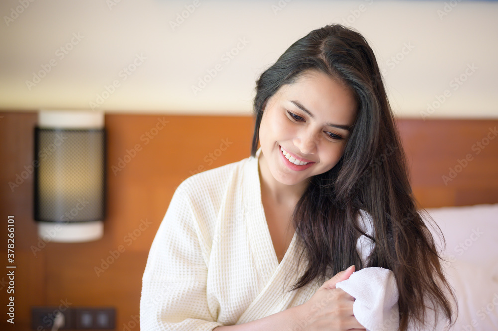 Smiling young woman wearing white bathrobe wiping her hair with towel after a shower in bedroom Smiling young woman wearing white bathrobe wiping her hair with towel after a shower in bedroom