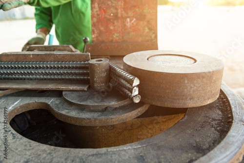 Worker hands in protective gloves working by using bender and cutting machine are cutting steel rebar rods for reinforcing concrete metal in the workshop yard at construction site