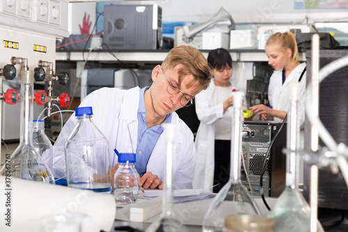 Focused student of Faculty of Biology performing experiments in university laboratory, writing results in test chart
