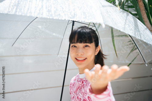 Asian woman in pink shirt holding transparent umbrella touching raindrop in sunny day.
