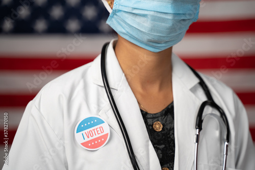 Konstfotografi Doctor or nurse medical mask and stethoscope wearing placing I voted sticker to her apron - concept of US election with US flag as background