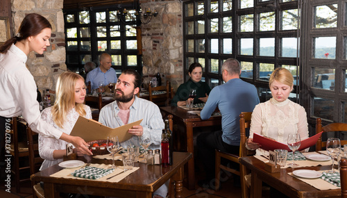 Charming young waiter receiving order from guests in country restaurant. High quality photo