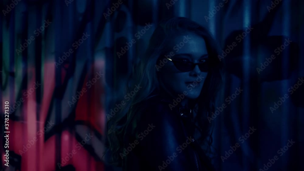 woman in sunglasses walking and looking at camera near wall with graffiti woman in sunglasses walking and looking at camera near wall with graffiti
