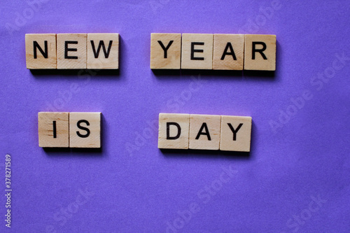 Words New Year is Day. Wooden blocks with inscription on purple background. The bulletin board. Concept of holiday-Christmas and New year. View from above. Copy space for Text. Christmas and New Year.
