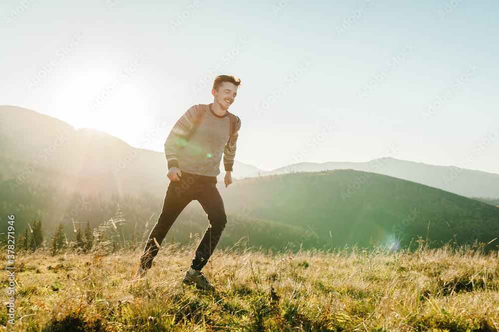 Tourist man with a backpack on top run and enjoying the sunset. Hipster walks in the autumn grass in the mountains on vacation. Holiday trip concept. World Tourism Day.