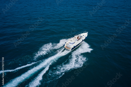 Girl in a swimsuit driving a large yacht in motion. White high-speed yacht in motion on blue water top view. High speed, Water splashing. Aerial view luxury motor boat. Back view © Berg