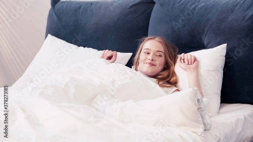Young woman lying in bed and stretching out 