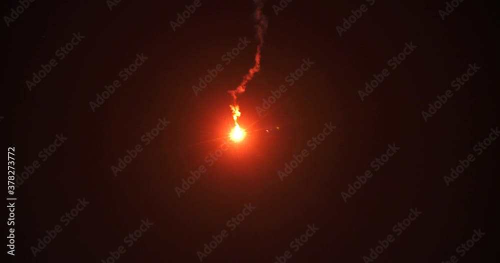 A bright red flare signal burns in the nighttime sky.