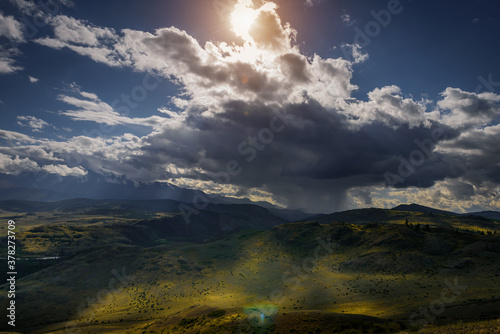 Mysterious mountain landscape with storm clouds hills and sun rays. Beautiful sky. Green grass on hills shimmers in the sunlight. Photo with tinting. Wallpaper for desktop or smartphone.