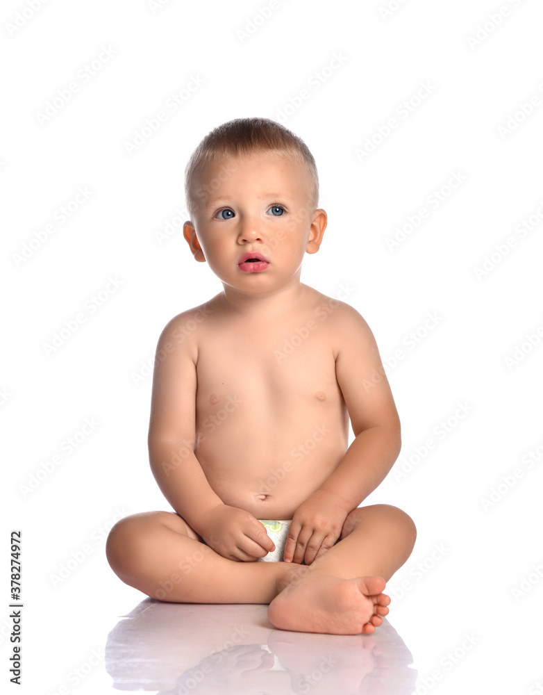 Curious attentive baby boy toddler naked in diaper sits on the floor and looks at upper corner Curious attentive baby boy toddler naked in diaper sits on the floor and looks at upper corner