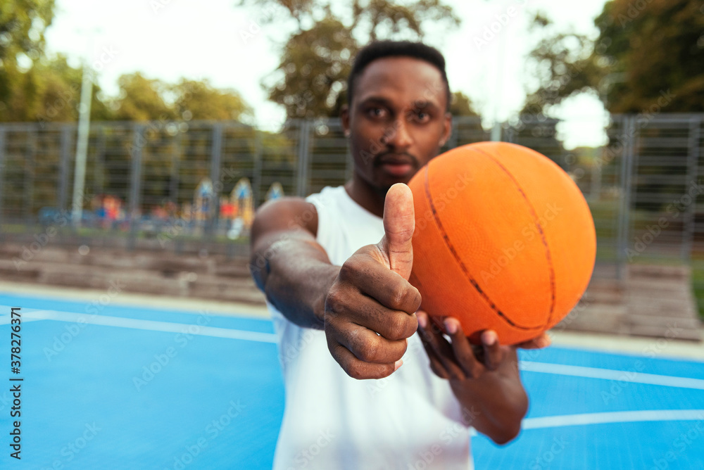 A man in a white T-shirt holds a basketball in front of him, shows everything ok with his hand. The concept of a healthy lifestyle. Selective focus, blurred image A man in a white T-shirt holds a basketball in front of him, shows everything ok with his hand. The concept of a healthy lifestyle. Selective focus, blurred image